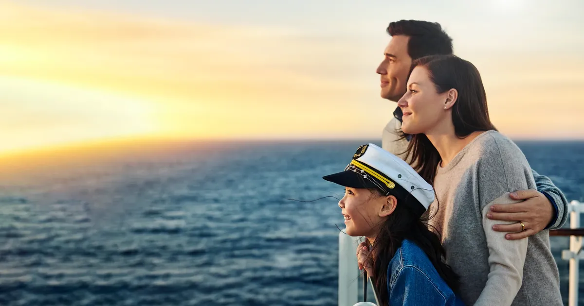 Two adults and a child looking across the ocean from a cruise ship at sunset