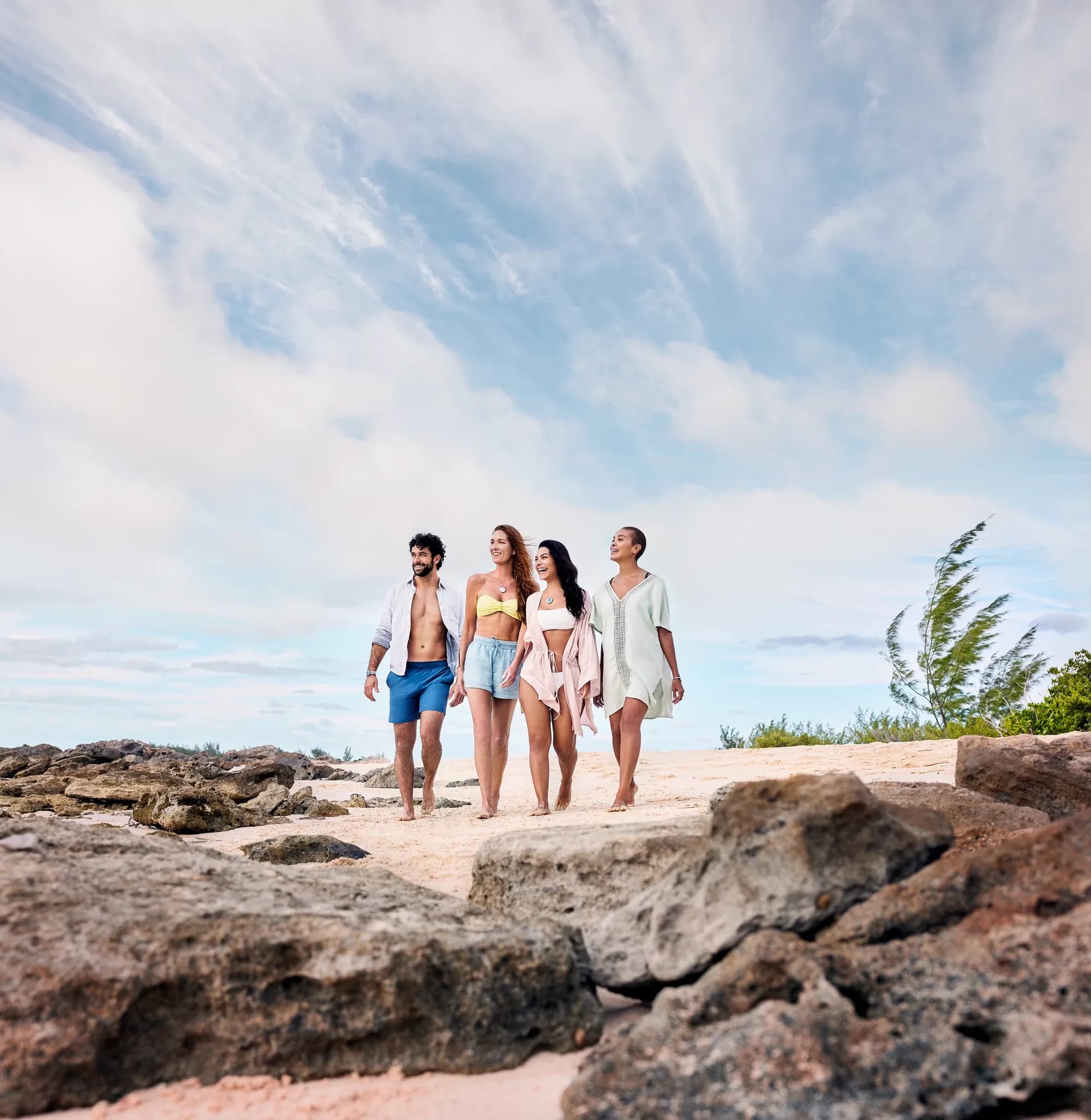 Four adults walking together on a rocky beach beneath a bright blue sky